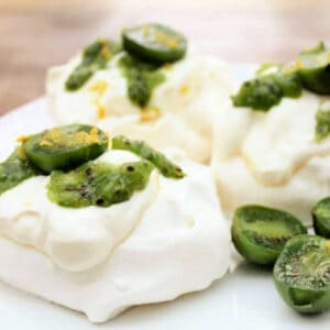 Small meringue nests filled with cream, topped with halved kiwi berries and lemon zest, on white plate.