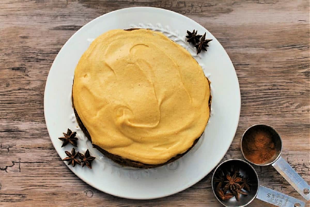 Overhead view of cake with pumpkin frosting on a white plate, with spices around.