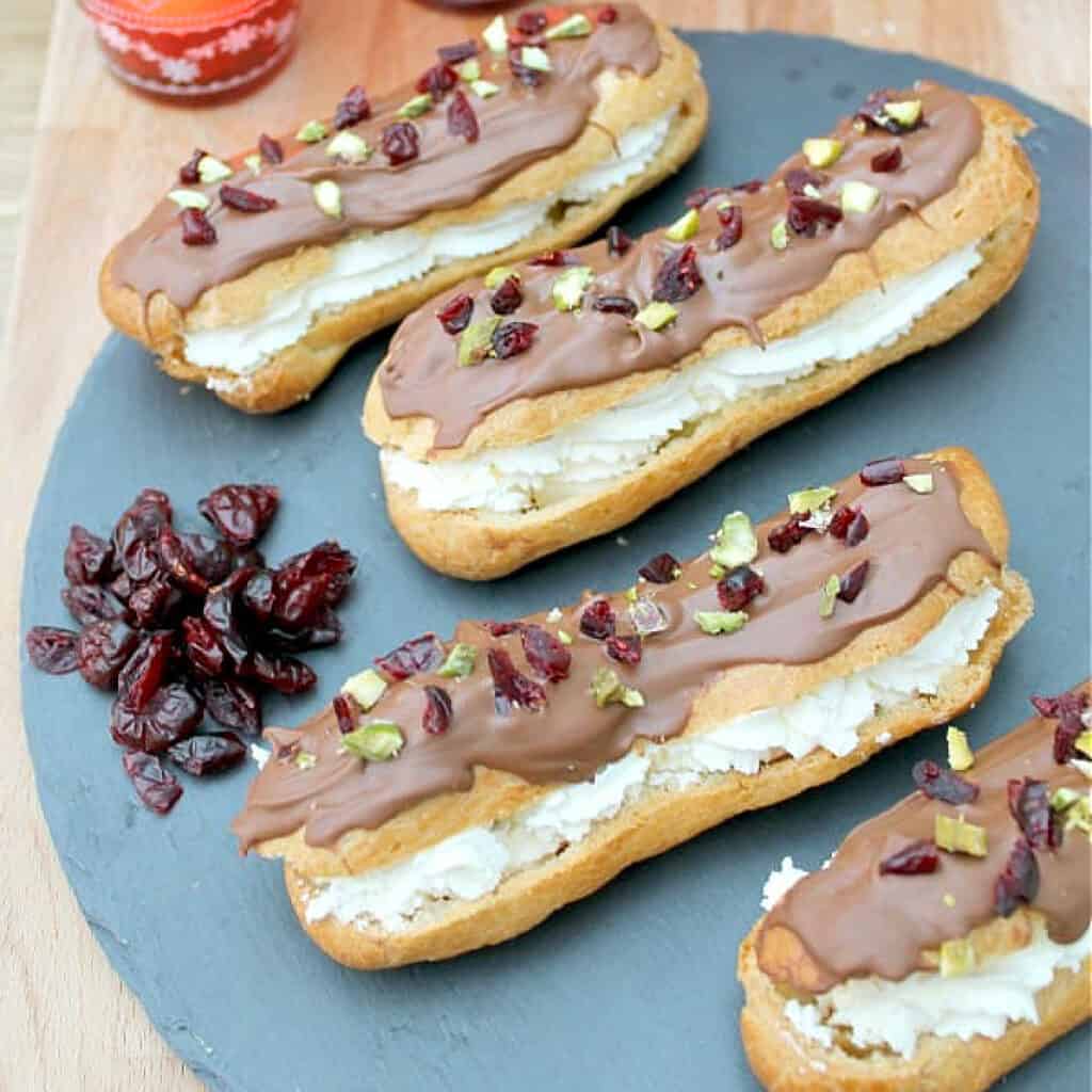Eclairs covered with chocolate on a slate board with a pile of cranberries.