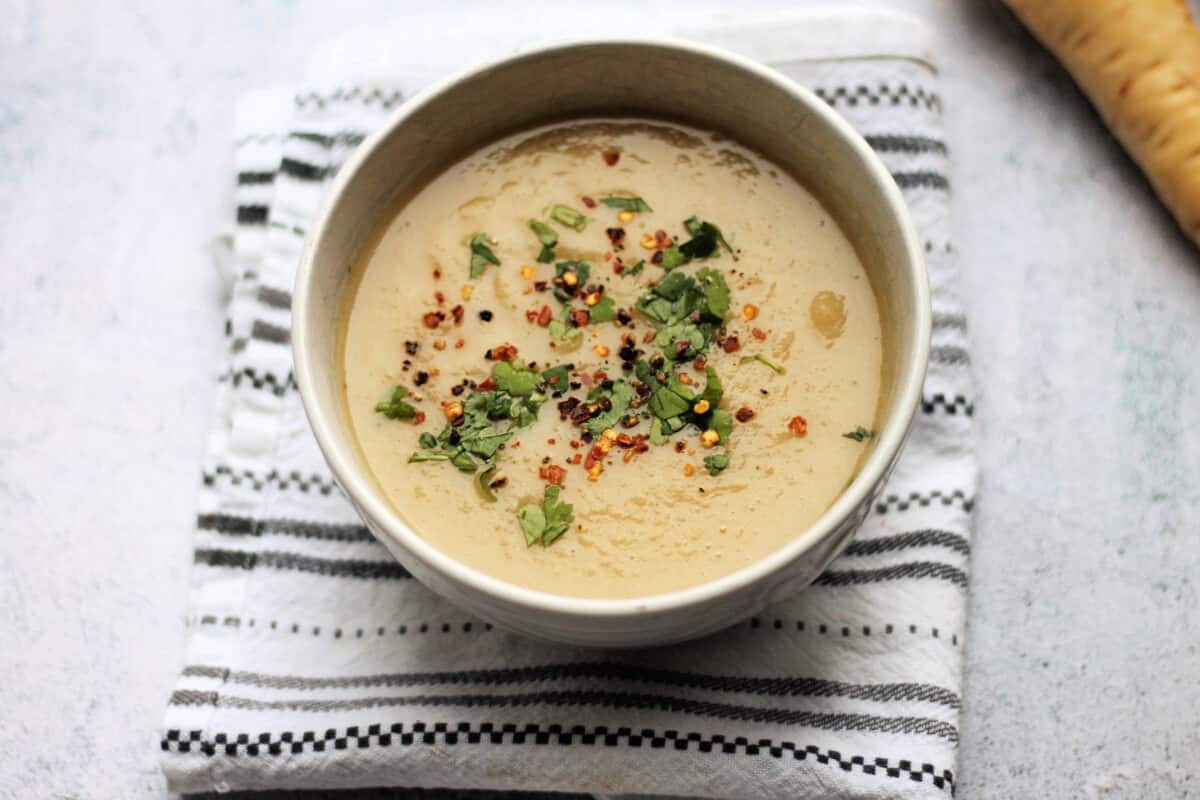 Bowl of soup on patterned cloth, with herbs.