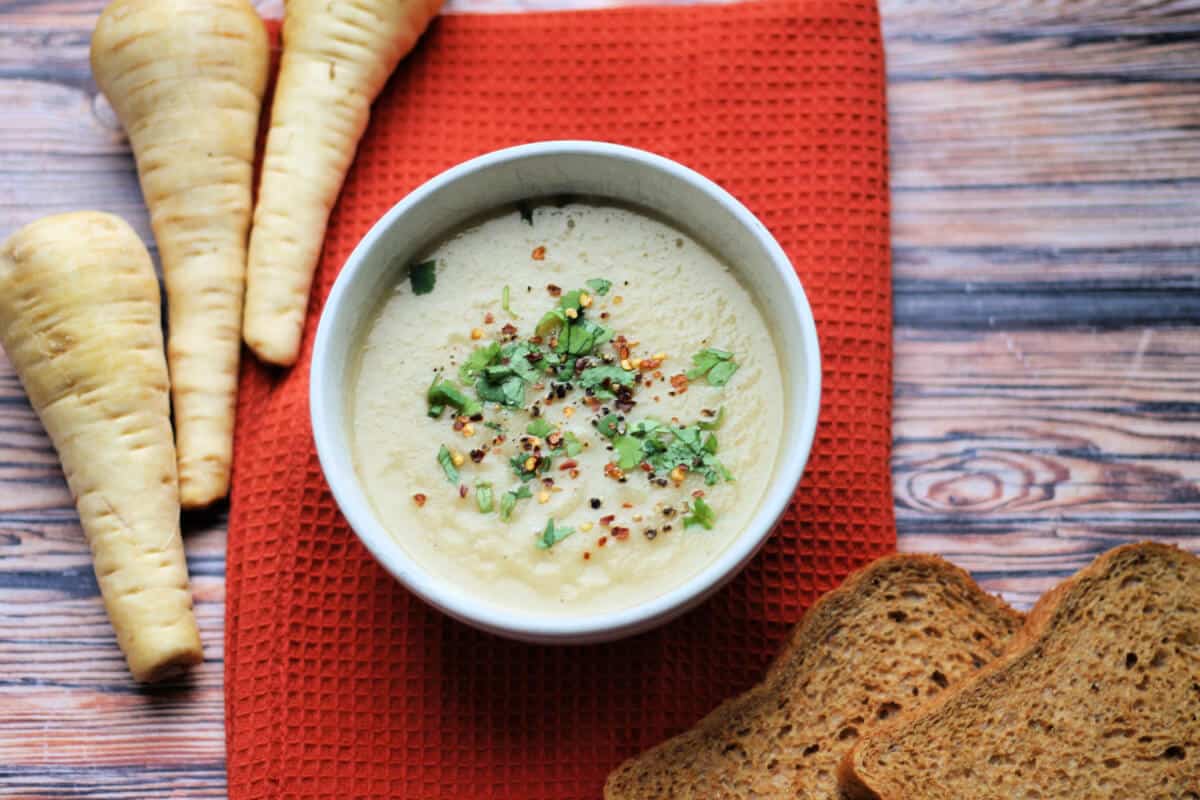 Bowl of soup with bread and raw parsnips next to it.