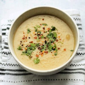 Bowl of parsnip soup garnished with herbs and crushed chilli, in a white bowl.