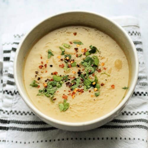 Bowl of parsnip soup garnished with herbs and crushed chilli, in a white bowl.