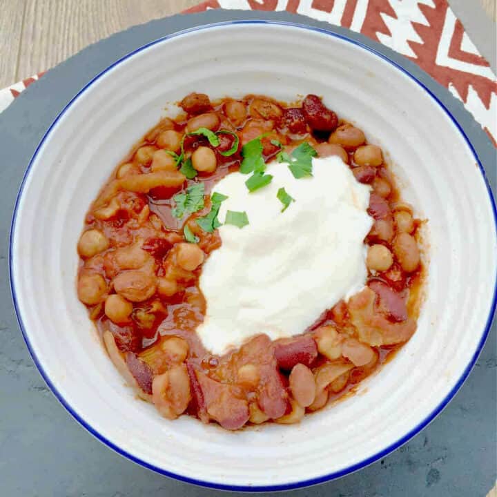 Bowl of bean stew topped with sour cream and fresh herbs.