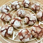 Icing sugar dusted crinkle cookies on round white rack.