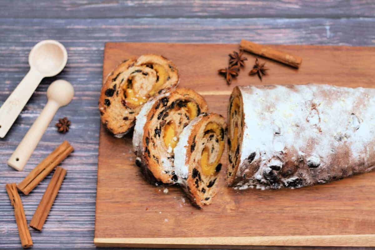 Fruit bread on a wooden chopping board with cinnamon sticks to the side.