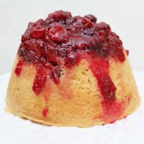 A steamed sponge pudding with cranberry sauce drizzled over it.