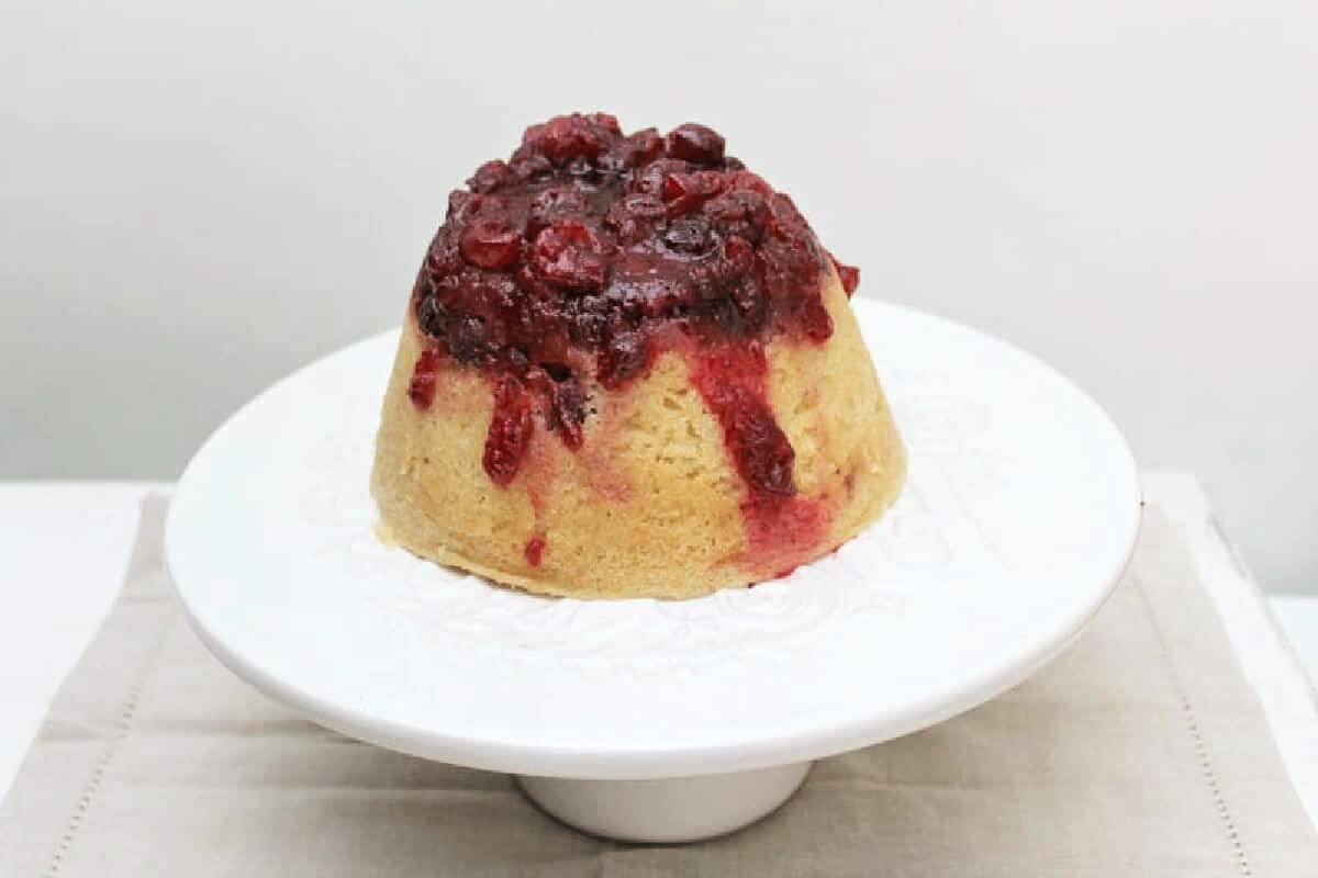 Steamed pudding on a cake stand, with cranberry compote poured over the top.