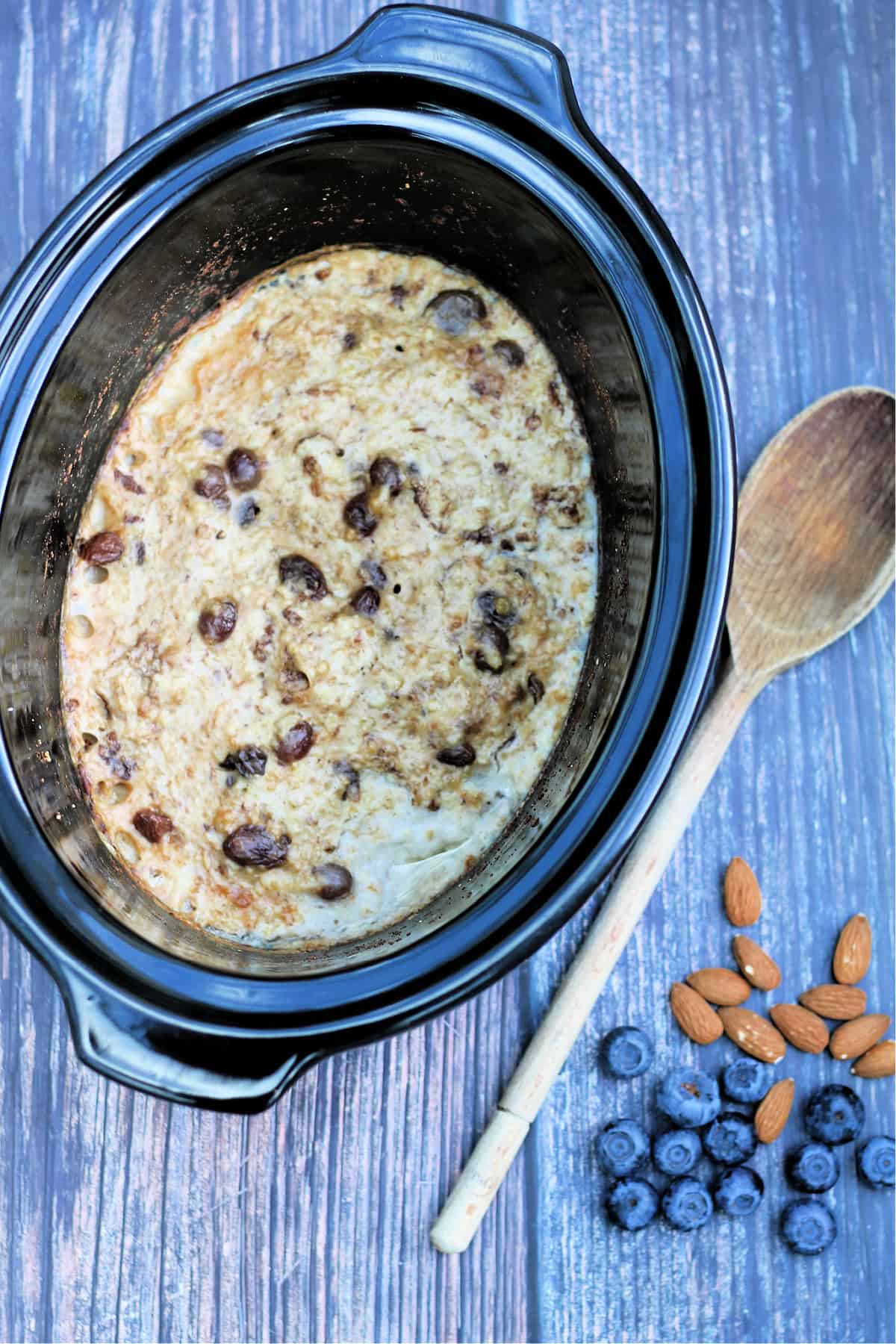 Slow cooker pot with oatmeal on a wooden background with a wooden spoon to the side.