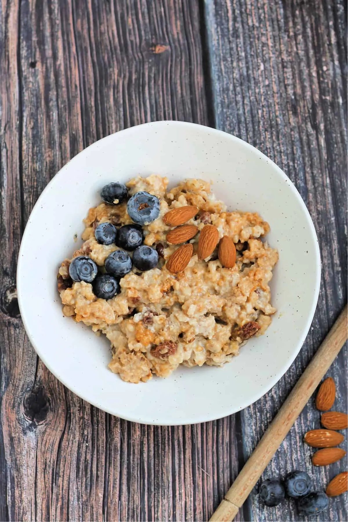 A white bowl of porridge/oatmeal with almonds and blueberries on top.