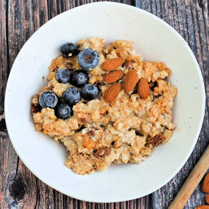Porridge/oatmeal in a white speckled bowl with a topping of blueberries and almonds.
