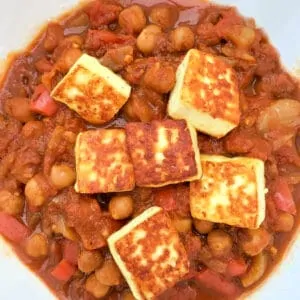 Close up of curry in a white bowl with paneer cheese cubes.