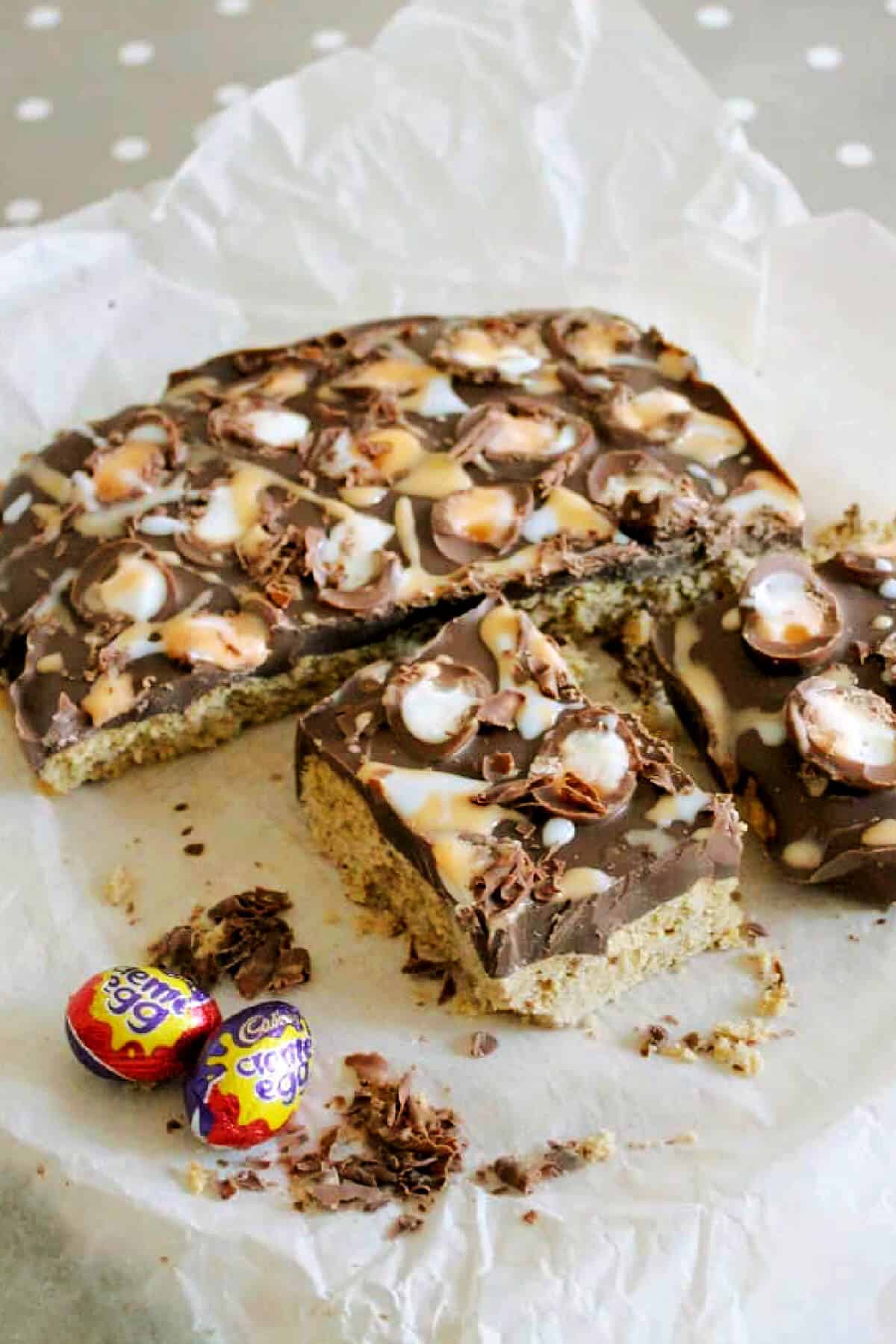 Creme egg topped chocolate cookie bars on baking paper, with wrapped Creme eggs.