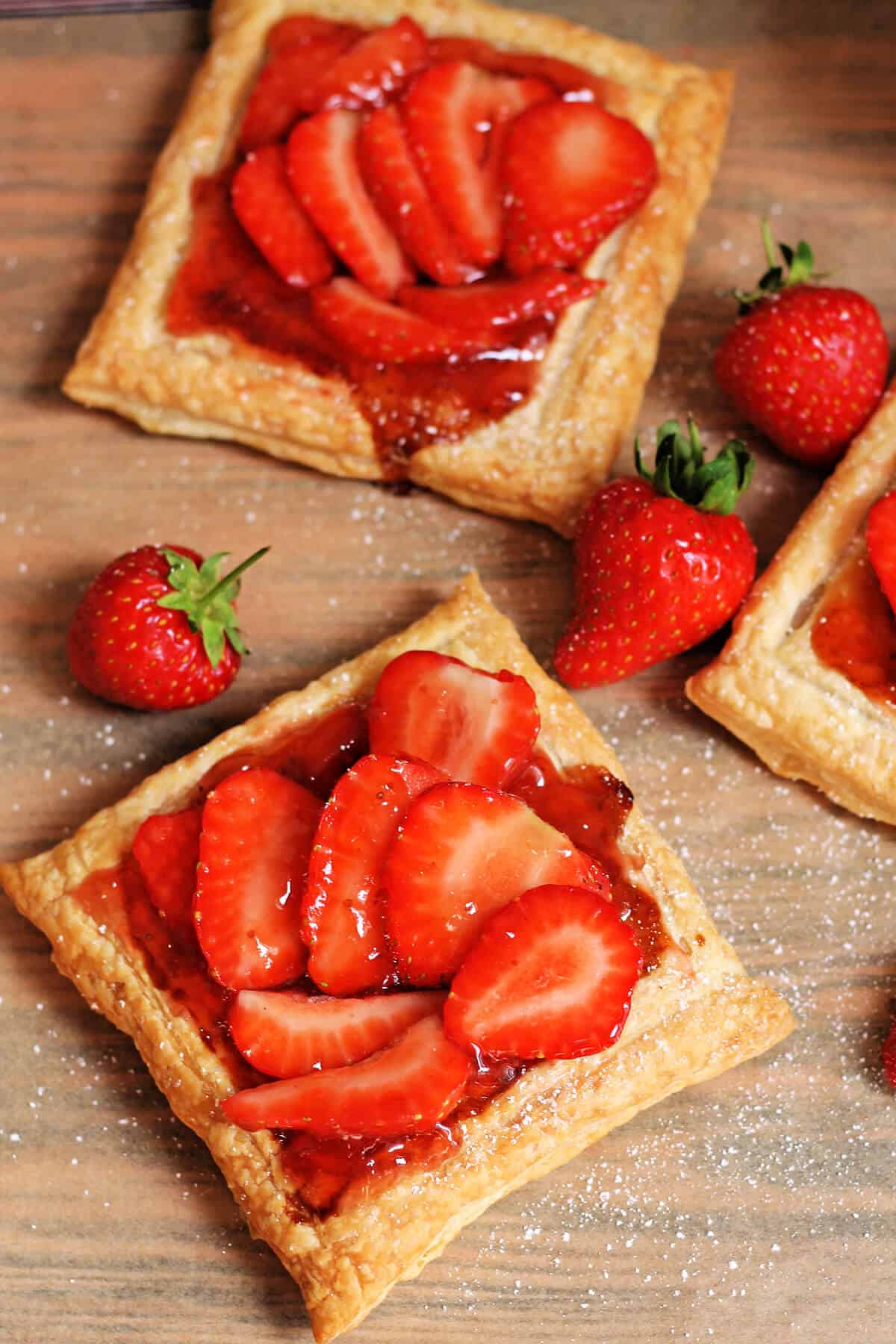 Two strawberry tarts topped with jam and strawberries.