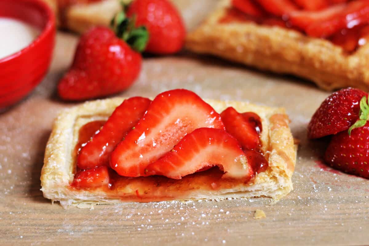 A strawberry tart cut in half showing the crispy pastry layer with jam and strawberry slices.