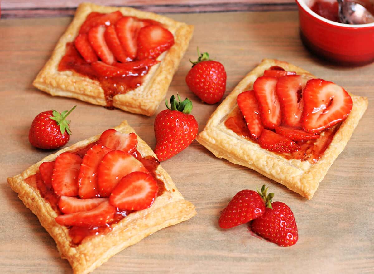 Strawberry tarts with jam and thinly sliced strawberries on puff pastry.