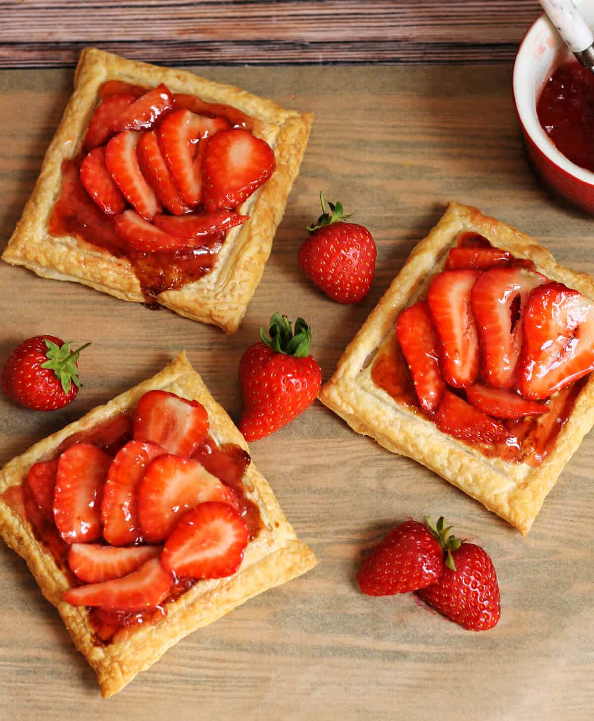 Three strawberry tarts made with jam and fresh strawberries.