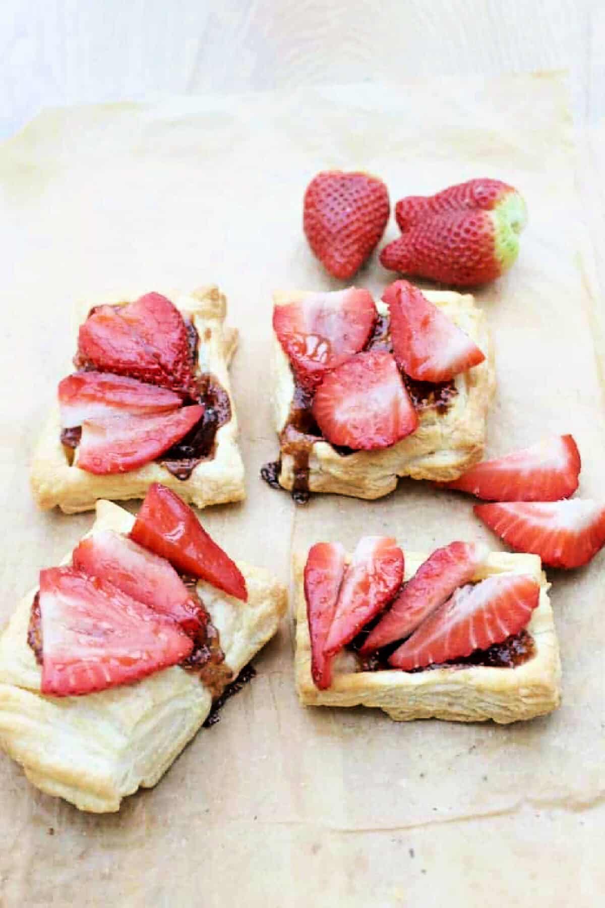 Strawberry puff pastry tart squares on baking paper.