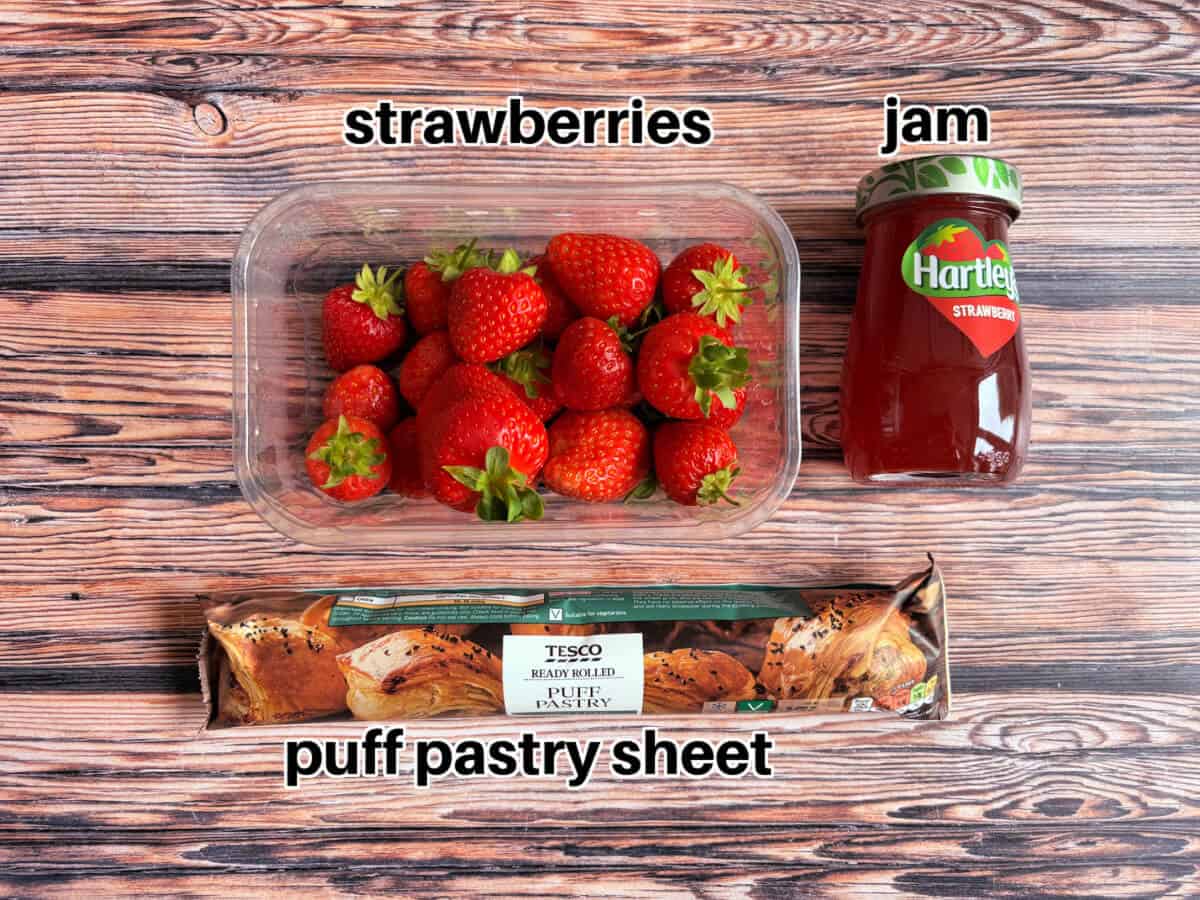 Strawberries, jar of jam and ready rolled pastry on a wooden table.