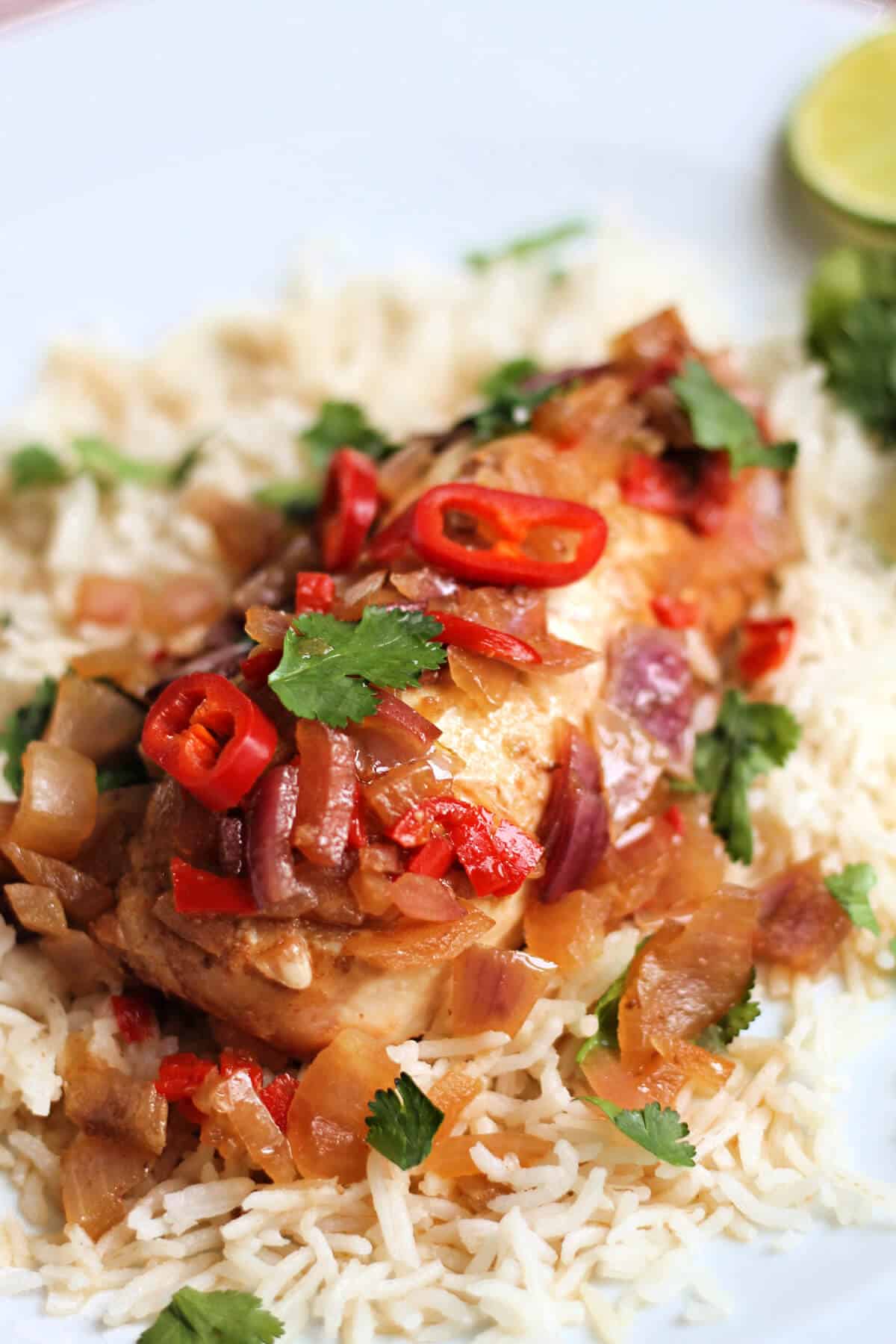 Chicken breast garnished with red chilli slices and fresh coriander leaves, on bed of rice.