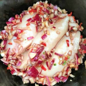 Chicken breasts with diced red onion and red chilli in slow cooker pot.