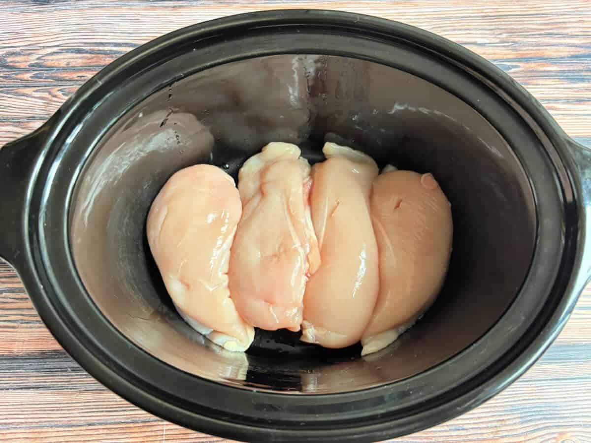 Four chicken breasts in a slow cooker dish.