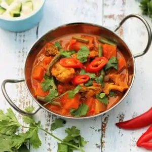 Vegetable curry topped with sliced red chillis and coriander in a metal bowl.