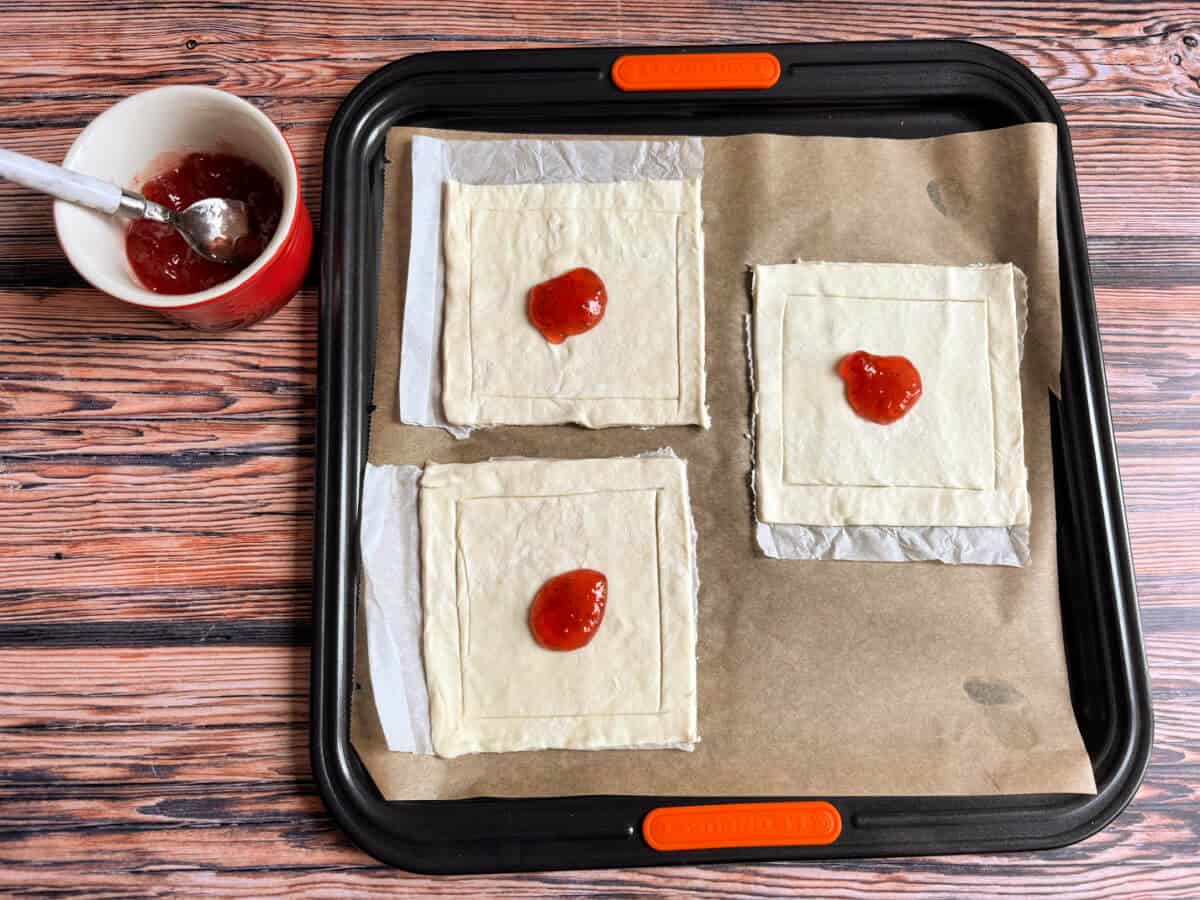 Pastry squares with a little jam in the centre, on a baking sheet.