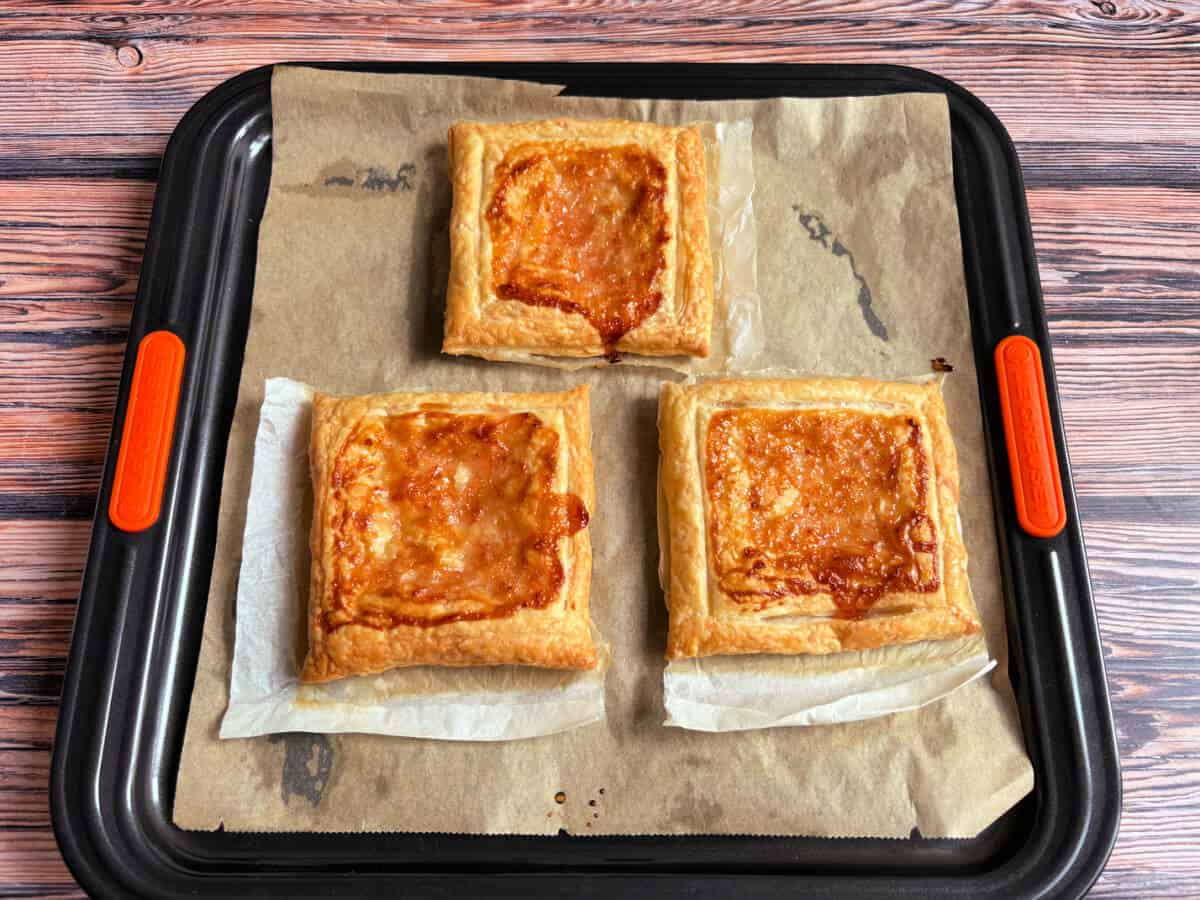 Three baked puff pastry squares with jam, on baking sheet.