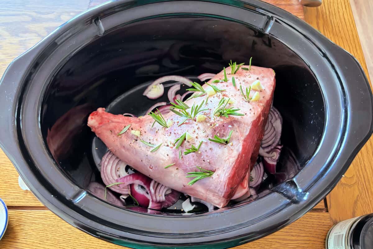 Lamb with garlic and rosemary in slashes in the meat, in slow cooker pot.