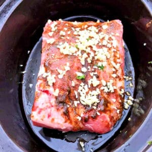 Lamb shoulder with spice rub in slow cooker pot.