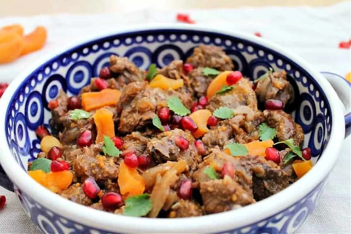 Close up of serving bowl with lamb stew with apricots, pomegranate seeds and herbs.