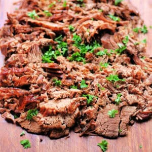 Beef brisket garnished with herbs on a wooden. board.