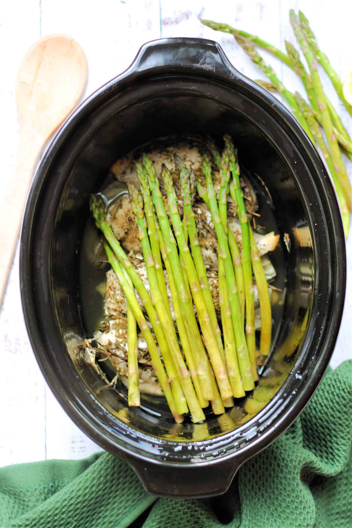 Chicken with asparagus cooked on top of it in a pot.