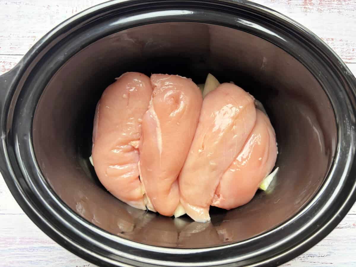 Chicken breasts in slow cooker pot.