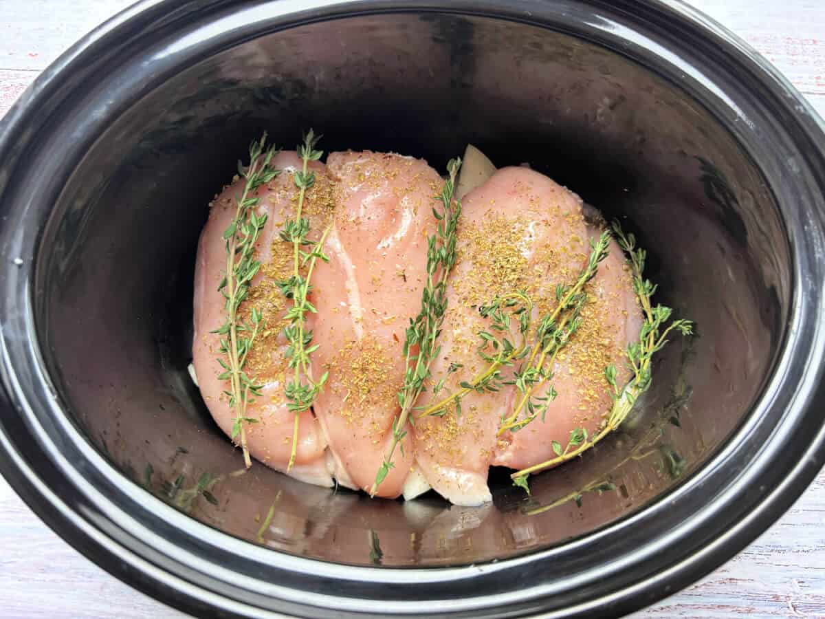 Chicken breast with herbs in slow cooker pot.