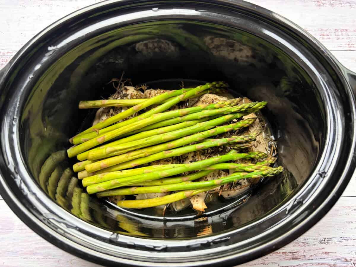 Asparagus on top of chicken in slow cooker pot.
