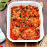 Chicken thighs and peppers in a white serving dish.