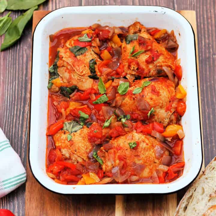 Chicken thighs and peppers in a white serving dish.