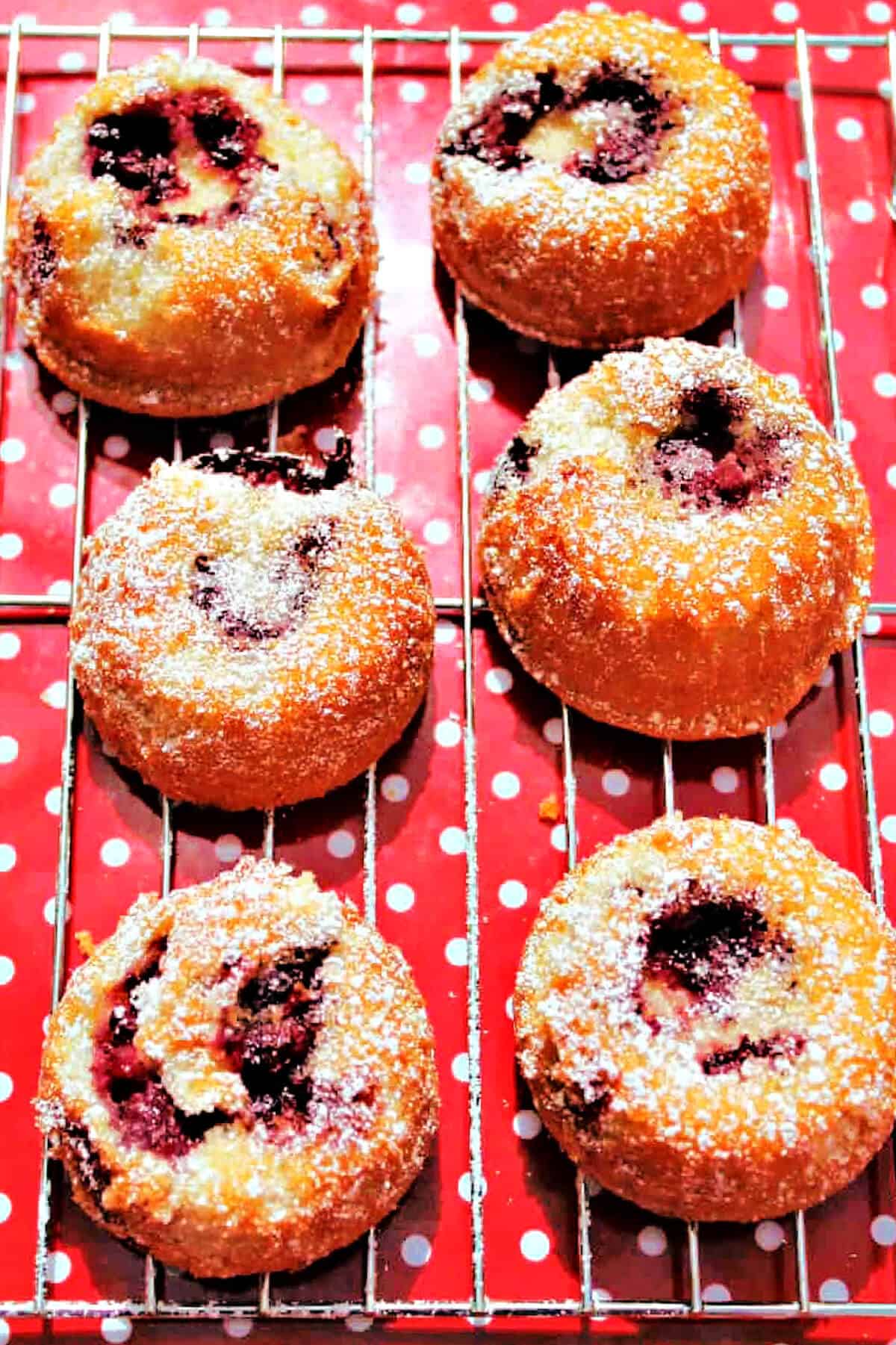 Little blackberry cake with fruit filling on a cooling rack and red tray.