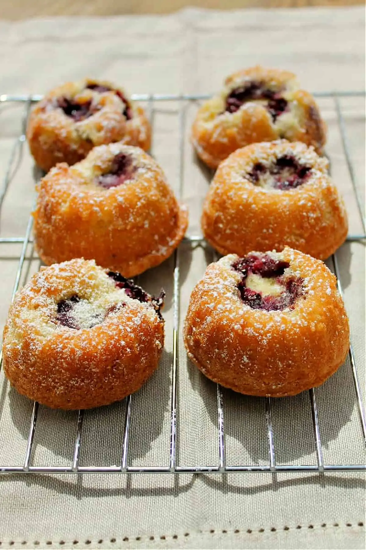 Six small cakes with blackberry filling on a metal cooling rack.