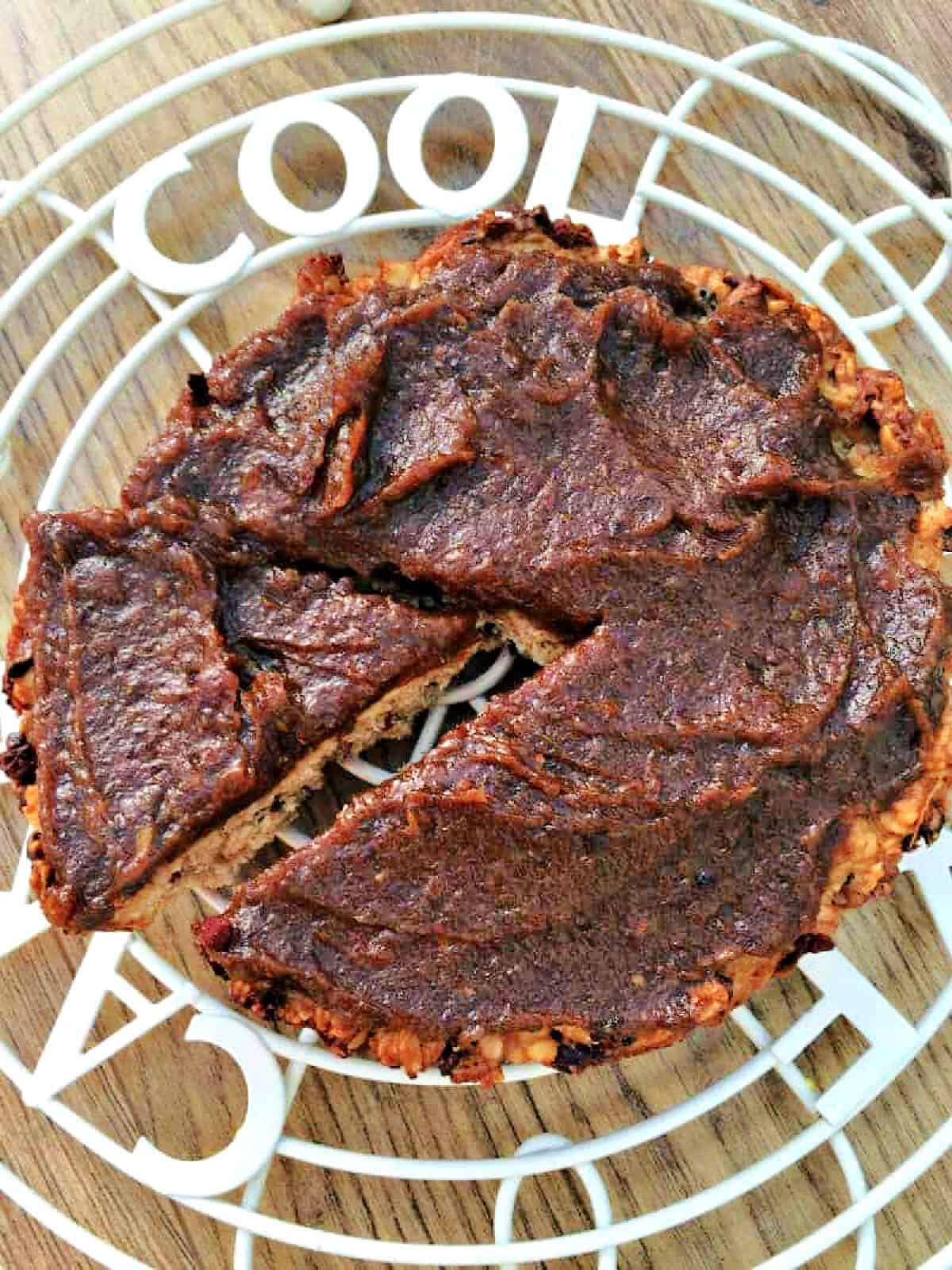 Round oat bar slice spread with date caramel on a rack, with one triangle cut out and pulled slightly out.