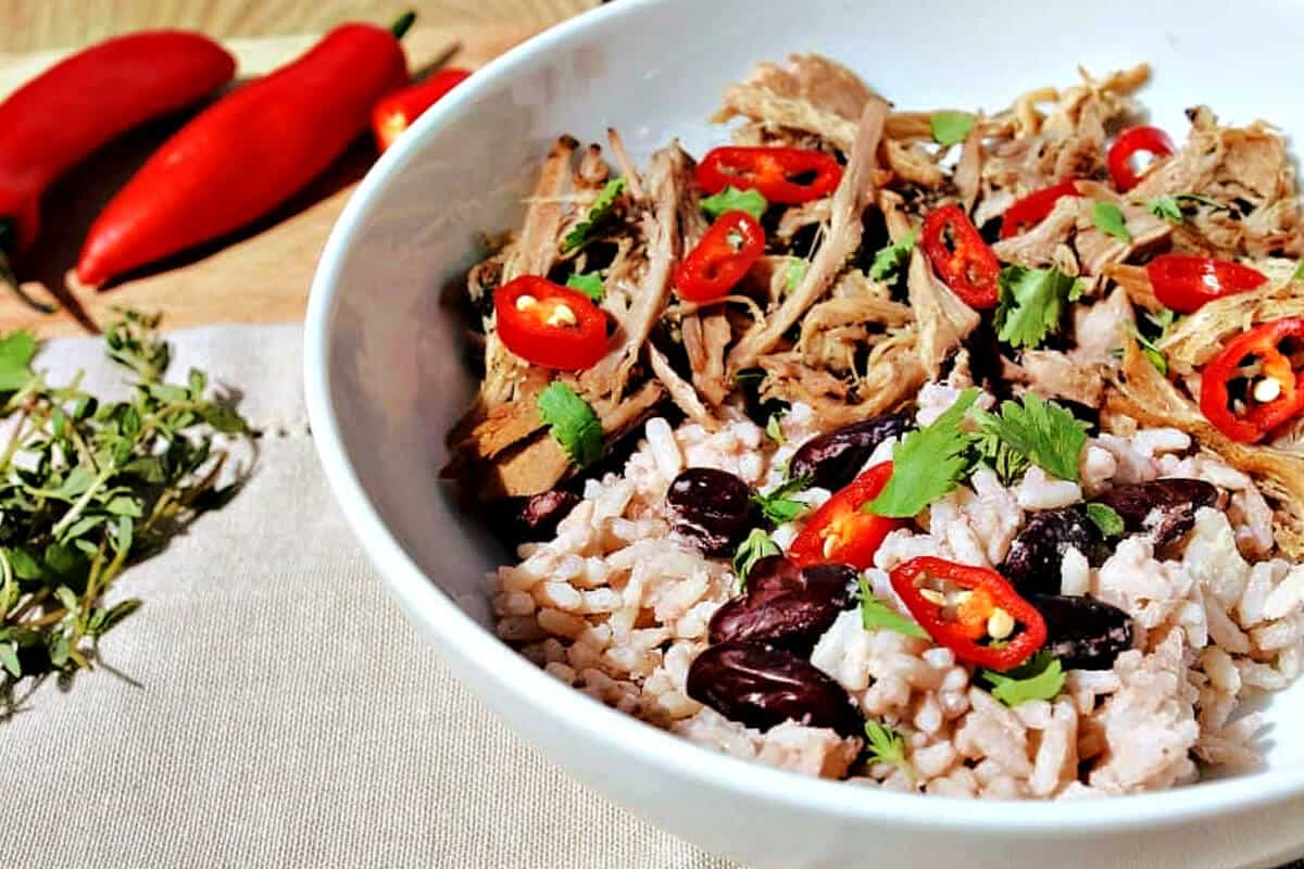 White bowl of pulled pork and rice, with thyme leaves and chilli to the side.