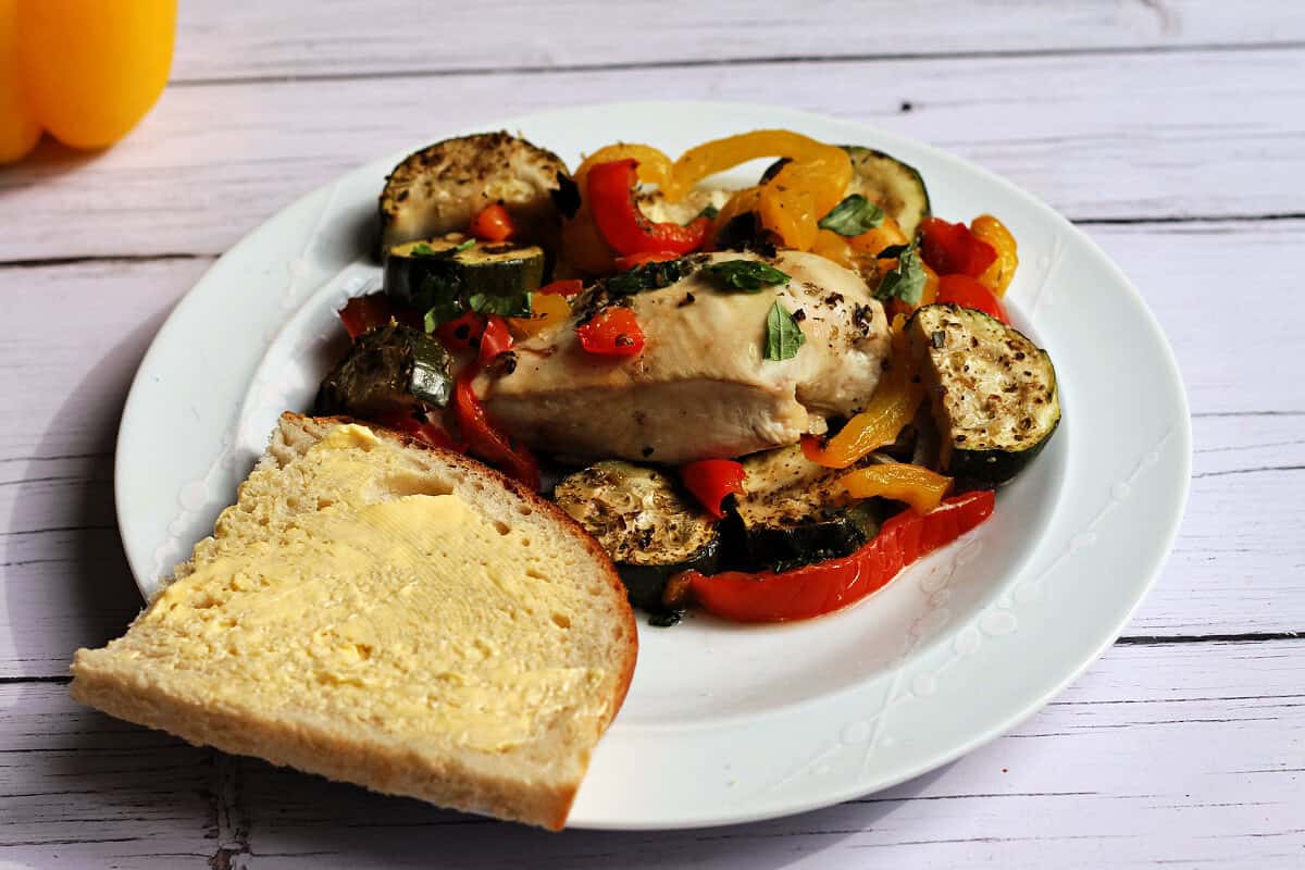 Plate with Mediterranean chicken breast with peppers and courgette, with a slice of buttered sourdough.