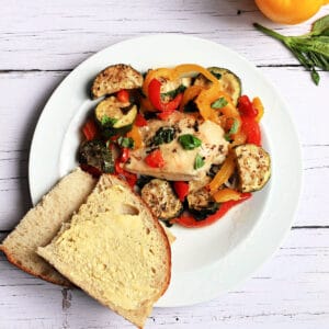Chicken breast with roasted vegetables and buttered bread on a white plate.