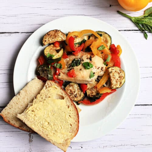 Chicken breast with roasted vegetables and buttered bread on a white plate.