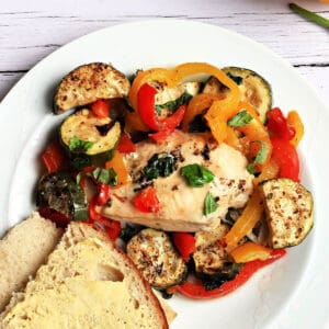 Chicken breast with roasted vegetables and buttered bread on a white plate.