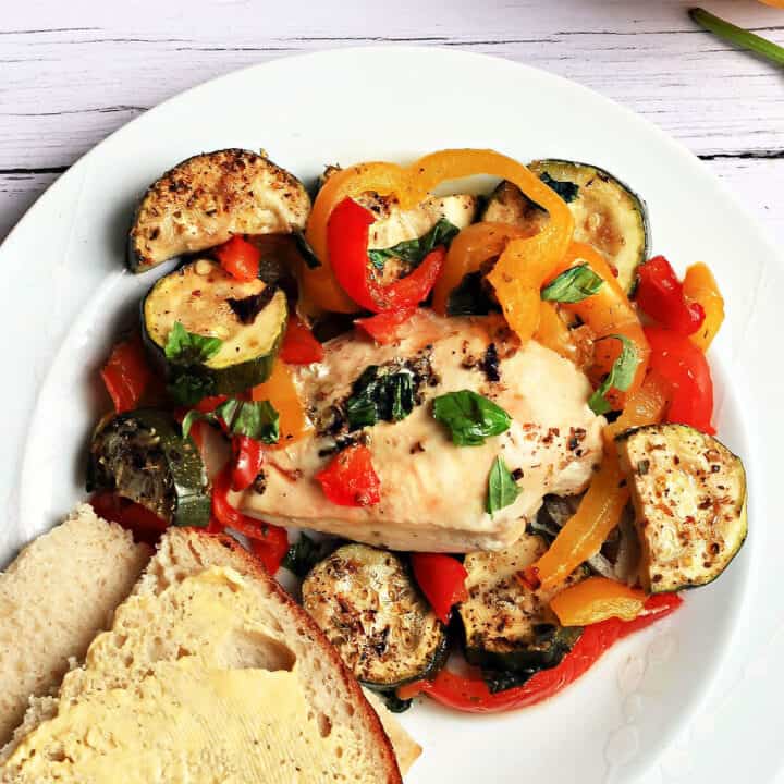 Chicken breast with roasted vegetables and buttered bread on a white plate.