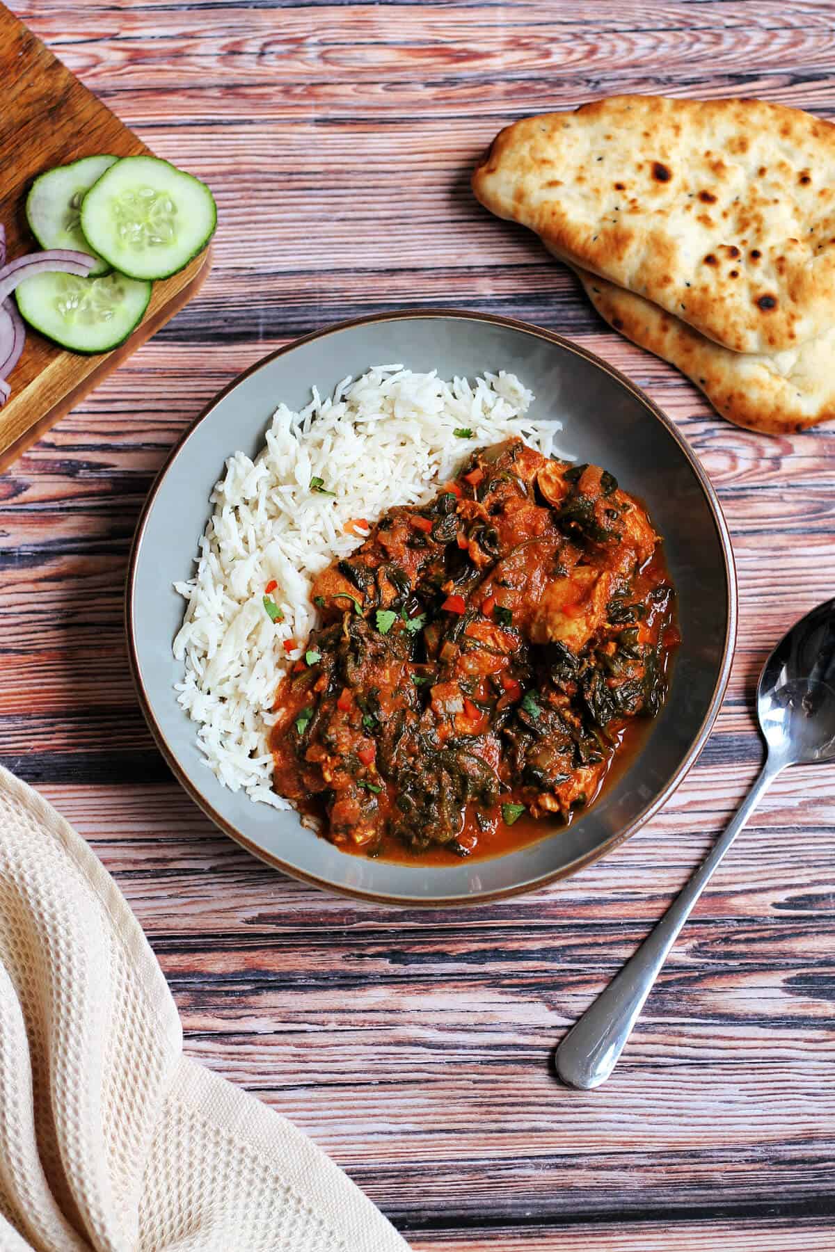 Dish of chicken spinach curry with rice, on wooden table.