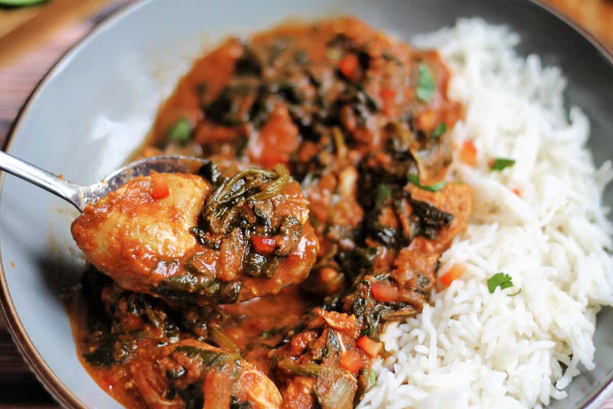 Chicken curry and rice in a grey bowl. Spoon lifting out a spoonful of the curry.
